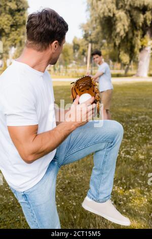 selective focus of man in leather glove posing while playing baseball with teenager son in park Stock Photo