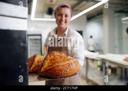 Proud happy female baker presnting fresh bread on a special flat shovel. Stock Photo
