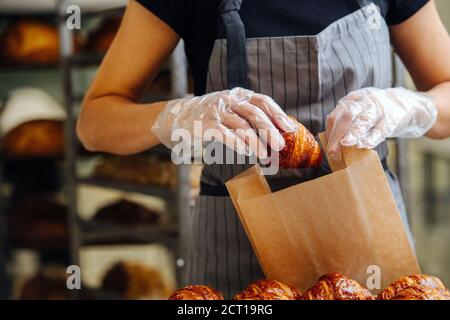 Seller placing freshly baked crispy golden croissants in a paper bag