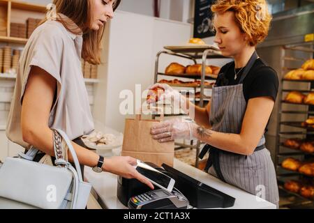 Baker placing freshly baked croissant in a paper bag for her client Stock Photo