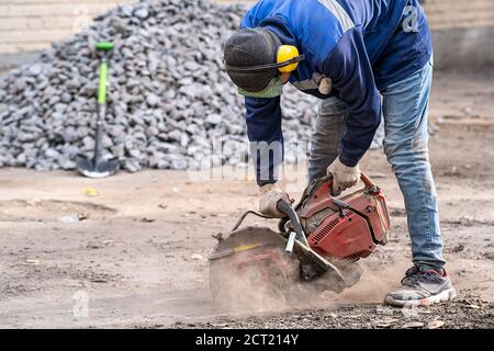 Construction worker in safety glasses and noise-canceling headphones at work. Cutting concrete floor for cable laying with a diamond cutting machine Stock Photo