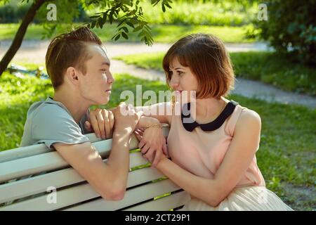 Young attractive woman is sitting on the bench in public park with her lover near during their meeting. Stock Photo