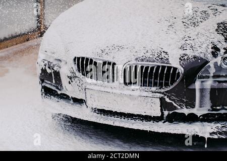 Black car getting wash with soap. Car washing concept. Automobile at carwash washed by water jet spray. Vehicle in foam. Stock Photo