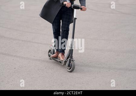 Low section of modern businessman in coat and pants riding electric scooter Stock Photo