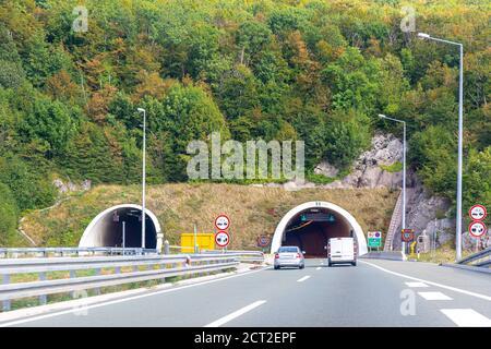 Entrance of tunnel in the mountains of Croatia. Colorful landscape with cars on highway and mountain forest with bright autumn foliage Stock Photo