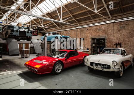 A Classic car garage at the Bicester Heritage Sunday scramble with a 1957 Chevrolet Corvette C1, a Ferrari 512BB, a Ferrari 250GTE and a Jaguar XJ Stock Photo
