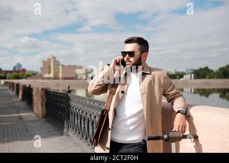 Bearded young businessman talking on smartphone while standing by riverside Stock Photo