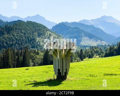 Abstract sculpture art on a green meadow with mountain range in distance Stock Photo