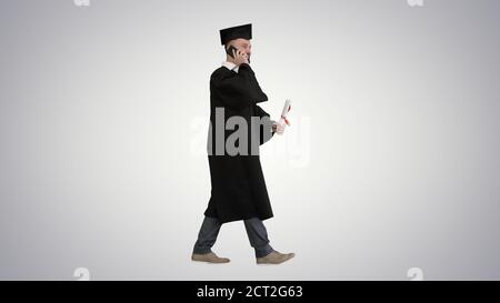Graduating student walking and making a call on gradient backgro Stock Photo