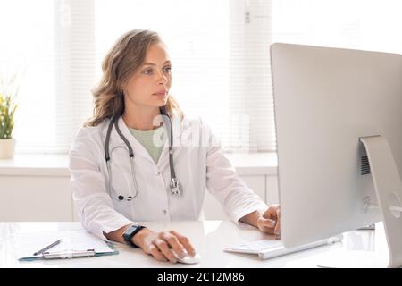Young serious clinician in whitecoat looking through data of her patients Stock Photo