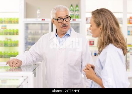 Senior owner of contemporary drugstore pointing at new medicaments in display Stock Photo