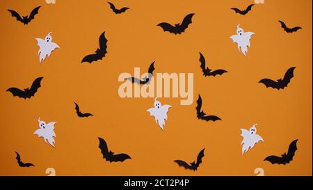 Halloween decoration concept - seamless pattern with black paper bats and ghosts on orange background, flat lay.Celebration of the dead. Stock Photo