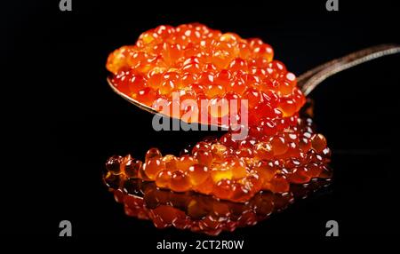 Red caviar in spoon on mirror surface. Stock Photo