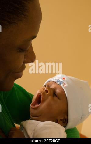 Sleepy six week old newborn baby boy wearing cap one month premature  held by mother reflex yawning vertical Stock Photo