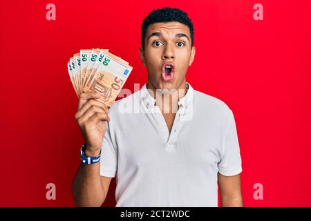 Young arab man holding 50 euro banknotes scared and amazed with open mouth for surprise, disbelief face Stock Photo