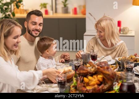 Happy mature blond female looking at her grandson sitting on knees of his father Stock Photo