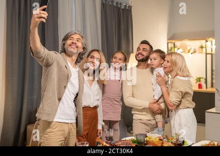 Happy mature man with smartphone making selfie with his big family at home Stock Photo