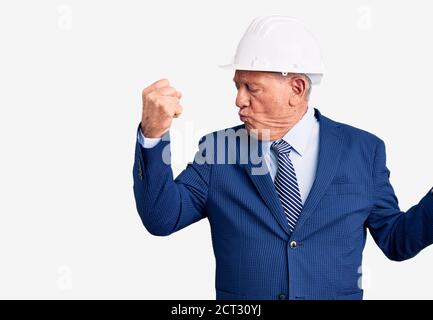 Senior handsome grey-haired man wearing suit and architect hardhat showing arms muscles smiling proud. fitness concept. Stock Photo