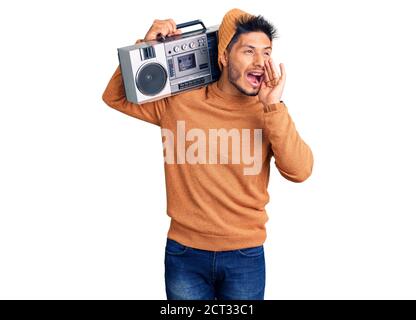 Handsome latin american young man holding boombox, listening to music shouting and screaming loud to side with hand on mouth. communication concept. Stock Photo