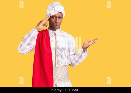 African handsome man wearing tradition sherwani saree clothes confused and annoyed with open palm showing copy space and pointing finger to forehead. Stock Photo