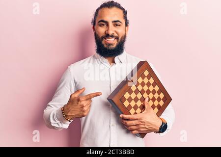 Young arab man holding chess smiling happy pointing with hand and finger Stock Photo