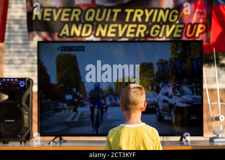 A boy watches the last stage of the Tour de France during a public viewing of the race.As Tadej Pogacar of Slovenia won this year’s Tour de France, people gathered in Komenda, his home town, to celebrate and watch the award ceremony on television. Stock Photo