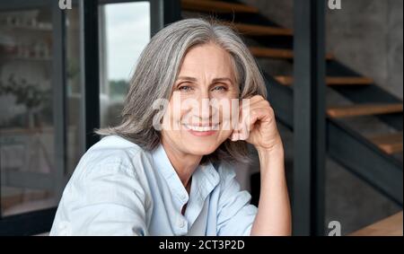 Smiling mature middle aged woman sitting at workplace, portrait. Stock Photo