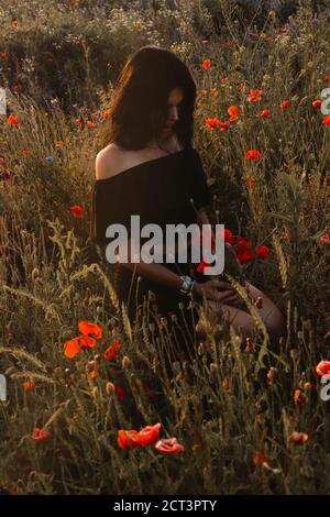 Summer nature atmospheric harmony. Beautiful brunette girl in long black dress with off shoulders and long dark hair cover face sitting half-turned wi Stock Photo