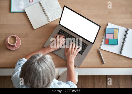Mature middle aged woman using laptop computer sitting at workplace, top view. Stock Photo