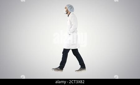 Walking doctor puting medical mask on on gradient background. Stock Photo