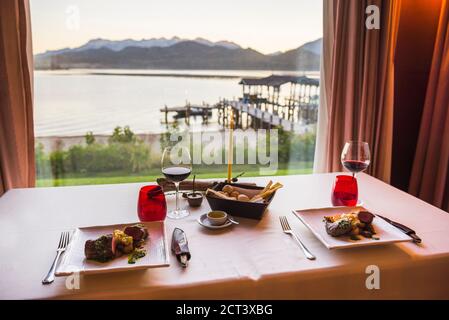 Table set up for dinner at a fine dining restaurant with a glass of red wine, delicious Argentinian steak and beautiful views of lakes and mountains, Patagonia, Argentina, South America Stock Photo