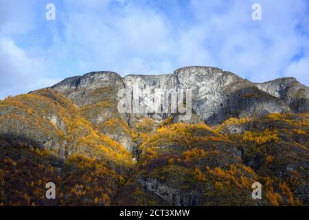 The large rocky mountains on the top of the mountain are snow white and  blue sky with clouds and the leaves turning yellow in autumn season. Stock Photo