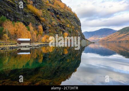 Small hut by the water and the mountains There are trees in which the leaves are turning orange during the fall reflecting in the beautiful water in t Stock Photo