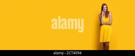 Monochrome photo of a caucasian woman with red hair posing in a dress on a yellow wall with free space advertising something Stock Photo