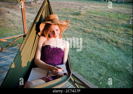 Tourist Writing her Diary in a Hammock at Bamboo Accommodation in Vang Vieng, Laos, Southeast Asia Stock Photo