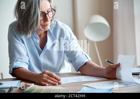 Mature older elegant woman fashion designer drawing sketches on table. Stock Photo