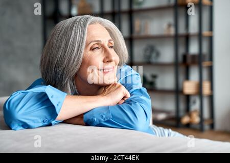 Happy relaxed mature old woman resting dreaming sitting on couch at home. Stock Photo