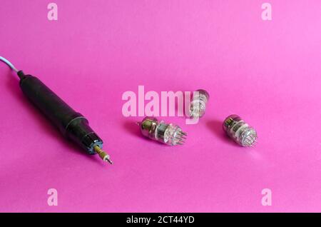 Group of random radio tubes and induction soldering iron on a pink background. Obsolete radio parts. Collecting or recycling. Selective focus. Stock Photo