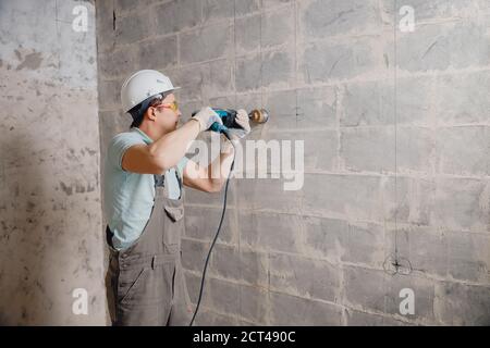 Builder worker pneumatic hammer drills hole in concrete brick wall with diamond crown for electric cable, socket, switch Stock Photo