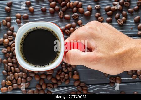 Hand holding a cup of coffee on a background of coffee beans lying on the table, top view. Stock Photo