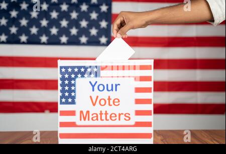 Close up of Hands placing vote inside the Ballot box with your vote matters printed with US flag as background - Concept of voter rights and US Stock Photo