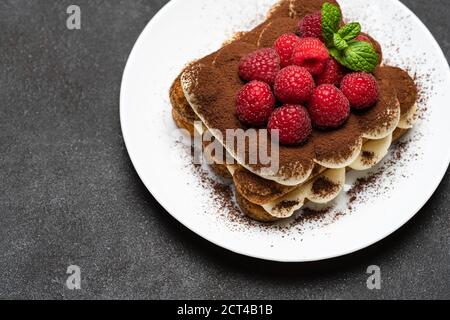 portion of Classic tiramisu dessert with raspberries on dark concrete background Stock Photo