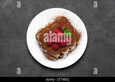 portion of Classic tiramisu dessert with raspberries on dark concrete background Stock Photo