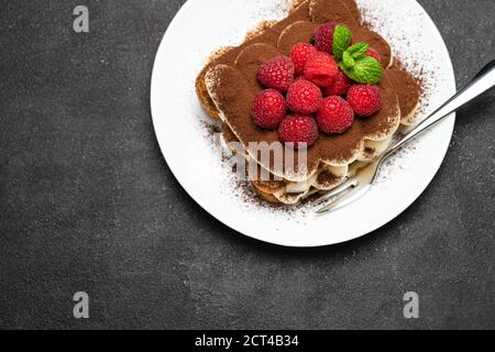 portion of Classic tiramisu dessert with raspberries on dark concrete background Stock Photo