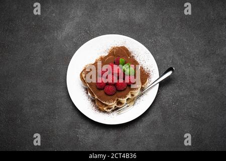 portion of Classic tiramisu dessert with raspberries on dark concrete background Stock Photo