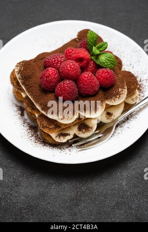 portion of Classic tiramisu dessert with raspberries on dark concrete background Stock Photo