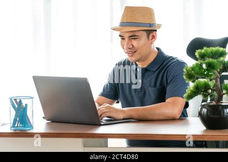 Online, remote job and lifestyle concept - happy Asian man with laptop computer working at home, Concept of technology communication Stock Photo