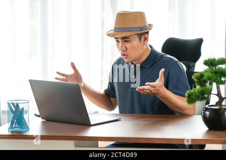 remote job, technology and people concept - stressed young asian man with laptop computer working at home, Concept of technology communication Stock Photo