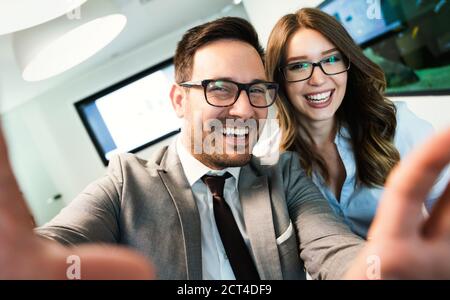Smiling business couple using smart phone while taking selfie in office. Stock Photo