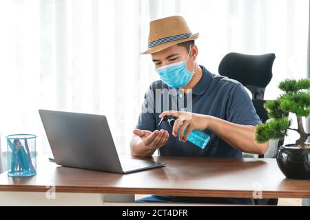 quarantine, happy asian man wearing face protective medical mask for protection from virus disease with laptop computer using hand sanitizer at home, Stock Photo